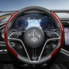 Close-up view of a black steering wheel with red carbon fiber texture covers, featuring a Mercedes-Benz logo.