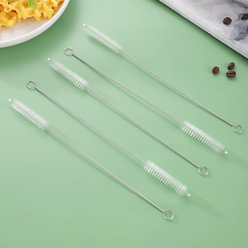 A set of reusable metal straws and bottle cleaning brushes displayed on a green surface.