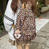 A person is wearing a leopard print nylon backpack with multiple pockets and a light gray sweater.