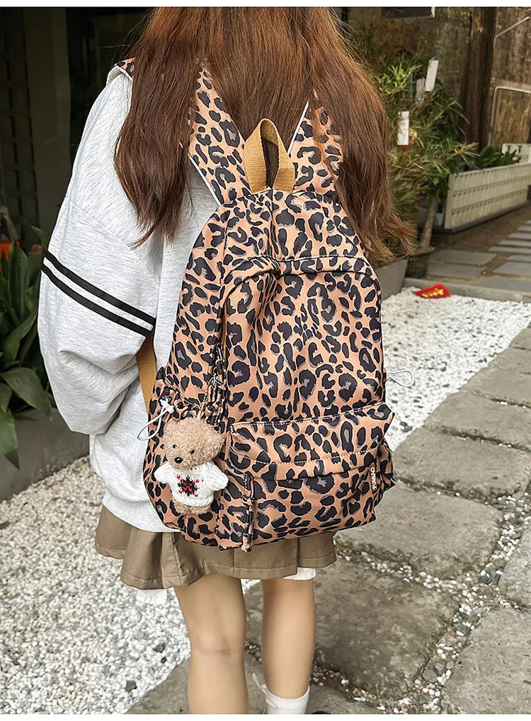 A person is wearing a leopard print nylon backpack with multiple pockets and a light gray sweater.