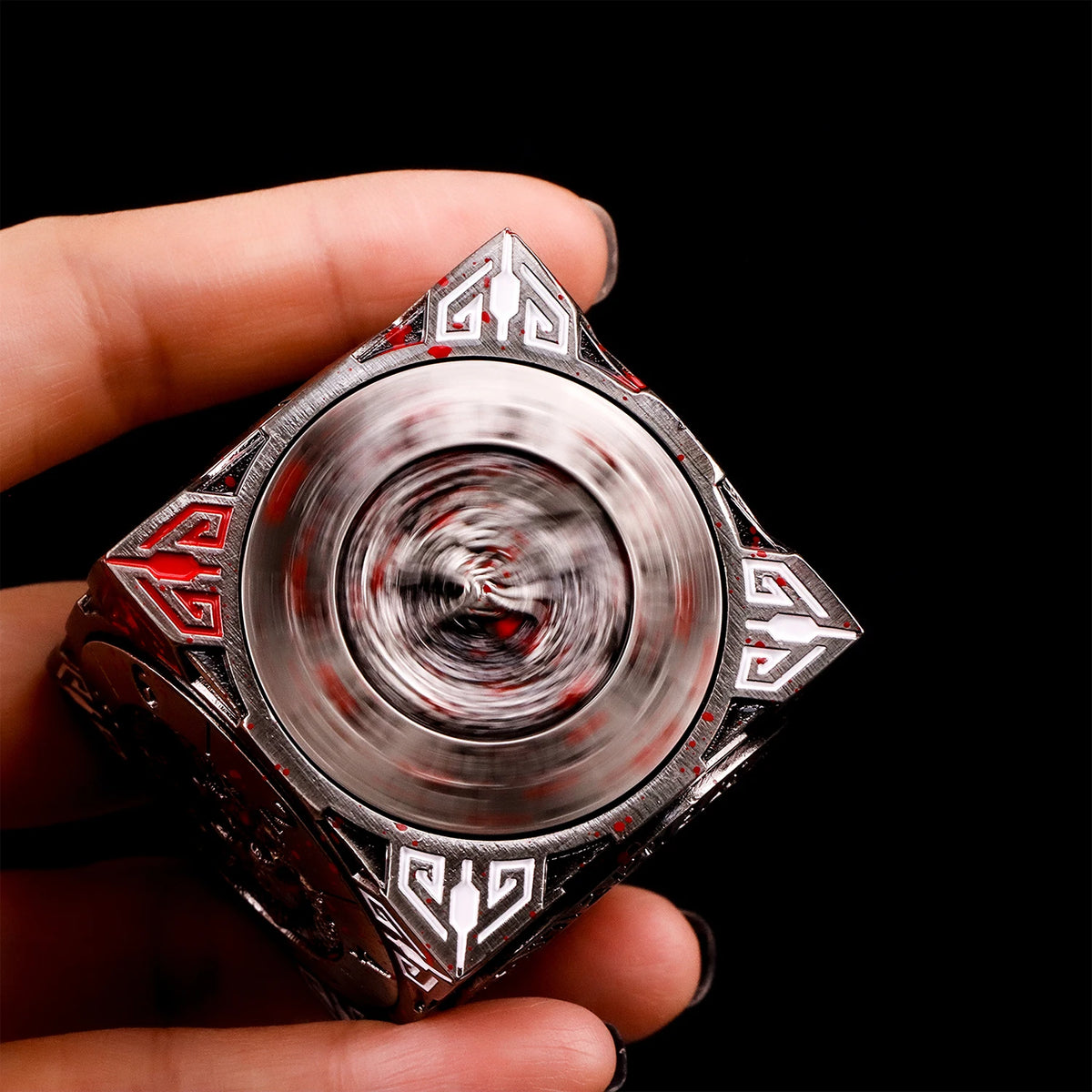 A hand holds a premium metal spinner dice cube with intricate patterns against a black background.