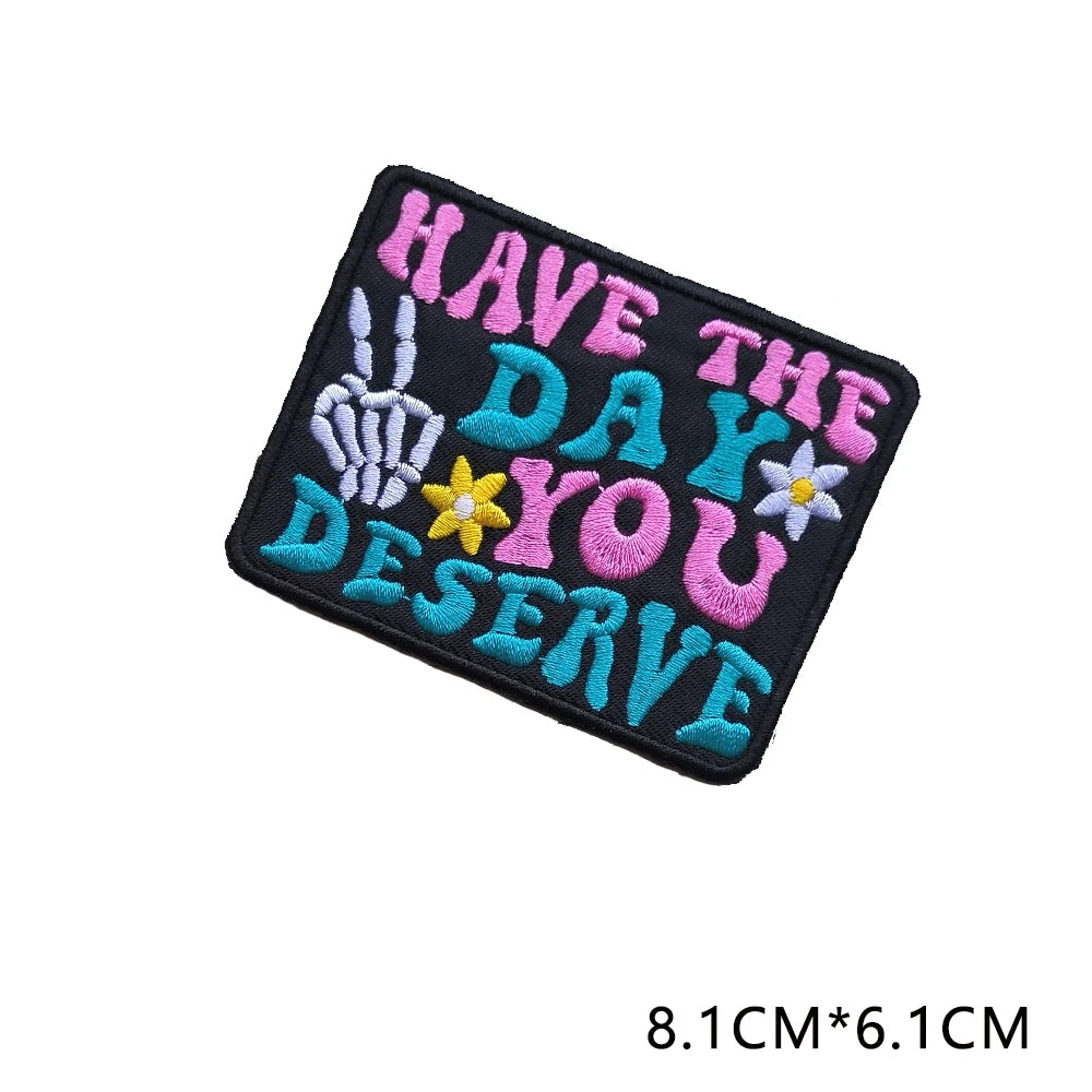 Black embroidered patch with the text HAVE THE DAY YOU DESERVE in colorful thread.