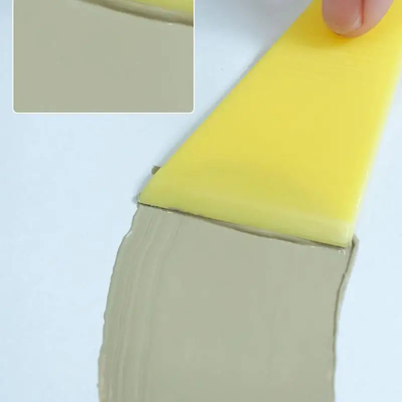 Un rotulador para reparar arañazos amarillo aplicando masilla de color claro en una superficie.