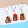 A set of three adorable capybara keychain charms in brown and orange tones displayed on a white plate.
