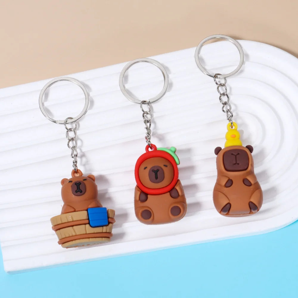 A set of three adorable capybara keychain charms in brown and orange tones displayed on a white plate.