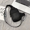 Black multi-function canvas chest bag with a strap lying on a gray fabric next to a laptop.