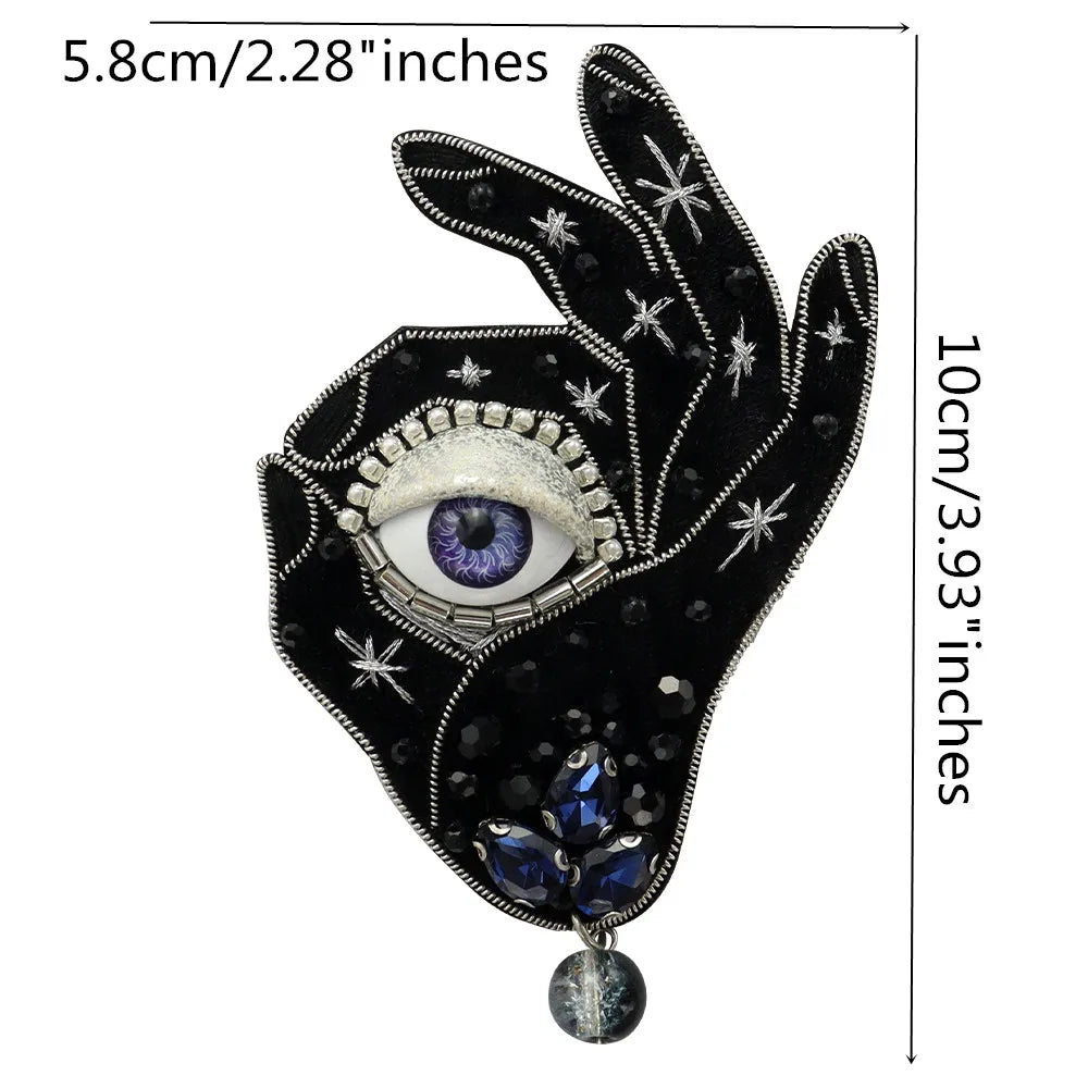 A black hand design featuring a large eye and blue gemstone pendant, suitable for clothing or craft projects.