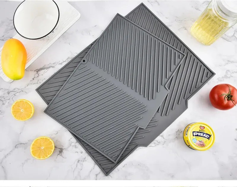 A gray silicone dish drying mat with textured ridges is shown next to citrus fruits and a jar of Spread.