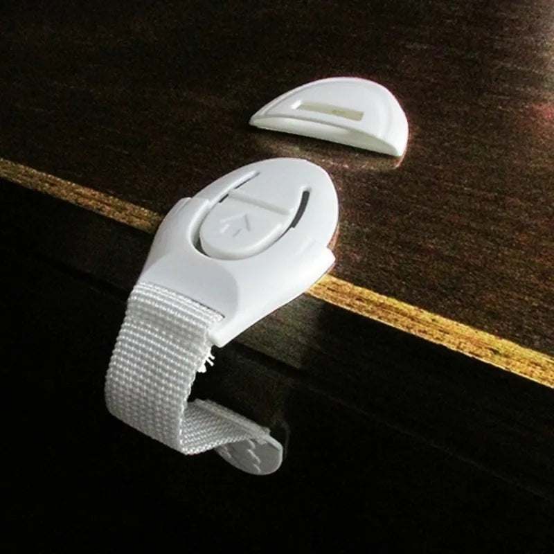 A white adhesive baby proofing latch for drawers, cupboards, and fridges, shown on a dark wooden surface.