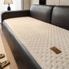 A dark leather sofa features a quilted beige plush cover with a non-slip backing.