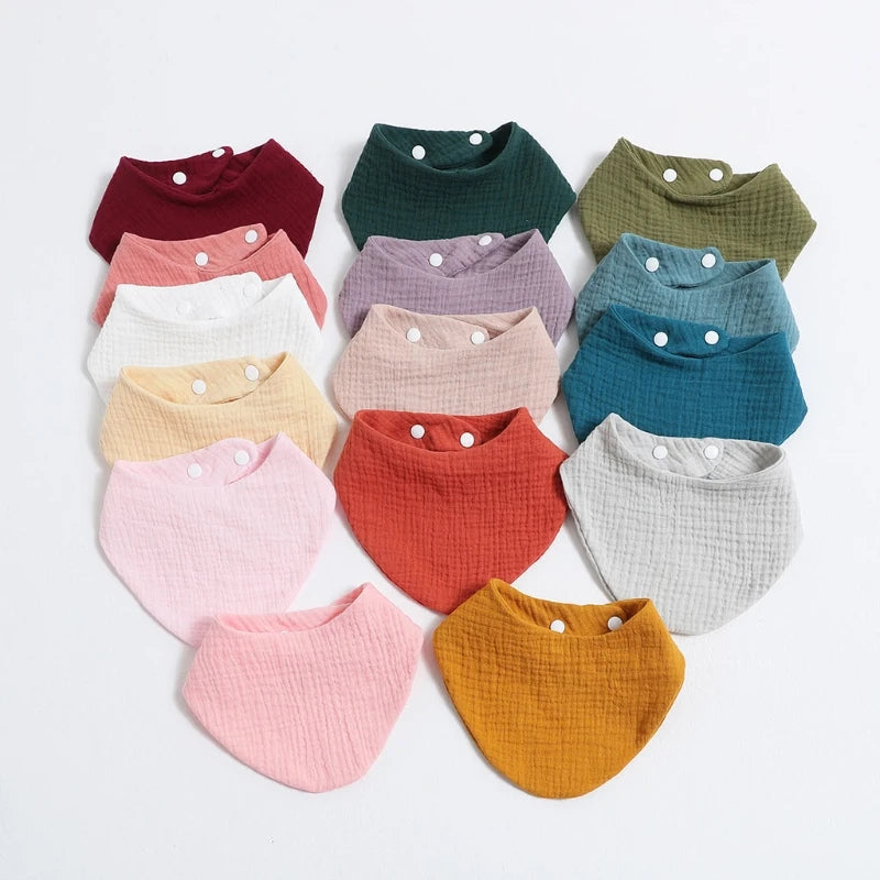A collection of colorful organic cotton muslin baby bibs in various shades including green, pink, yellow, and blue.