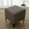 A beige geometric jacquard stretch ottoman cover placed on a wooden floor.