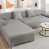 A modern gray plush velvet elastic sofa cover is shown on an L-shaped sectional with matching pillows.