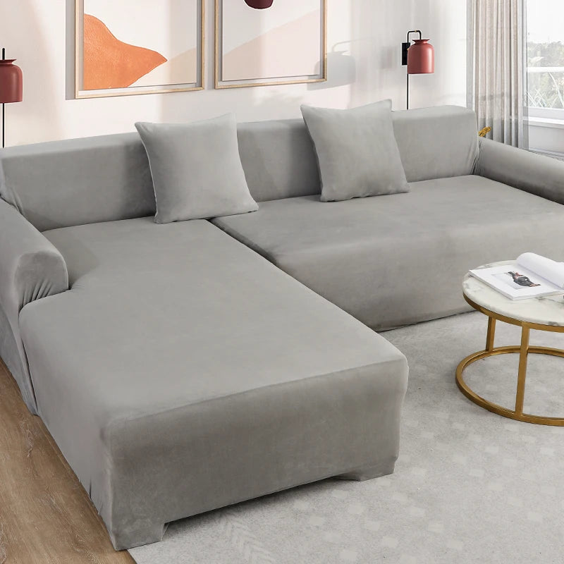 A modern gray plush velvet elastic sofa cover is shown on an L-shaped sectional with matching pillows.