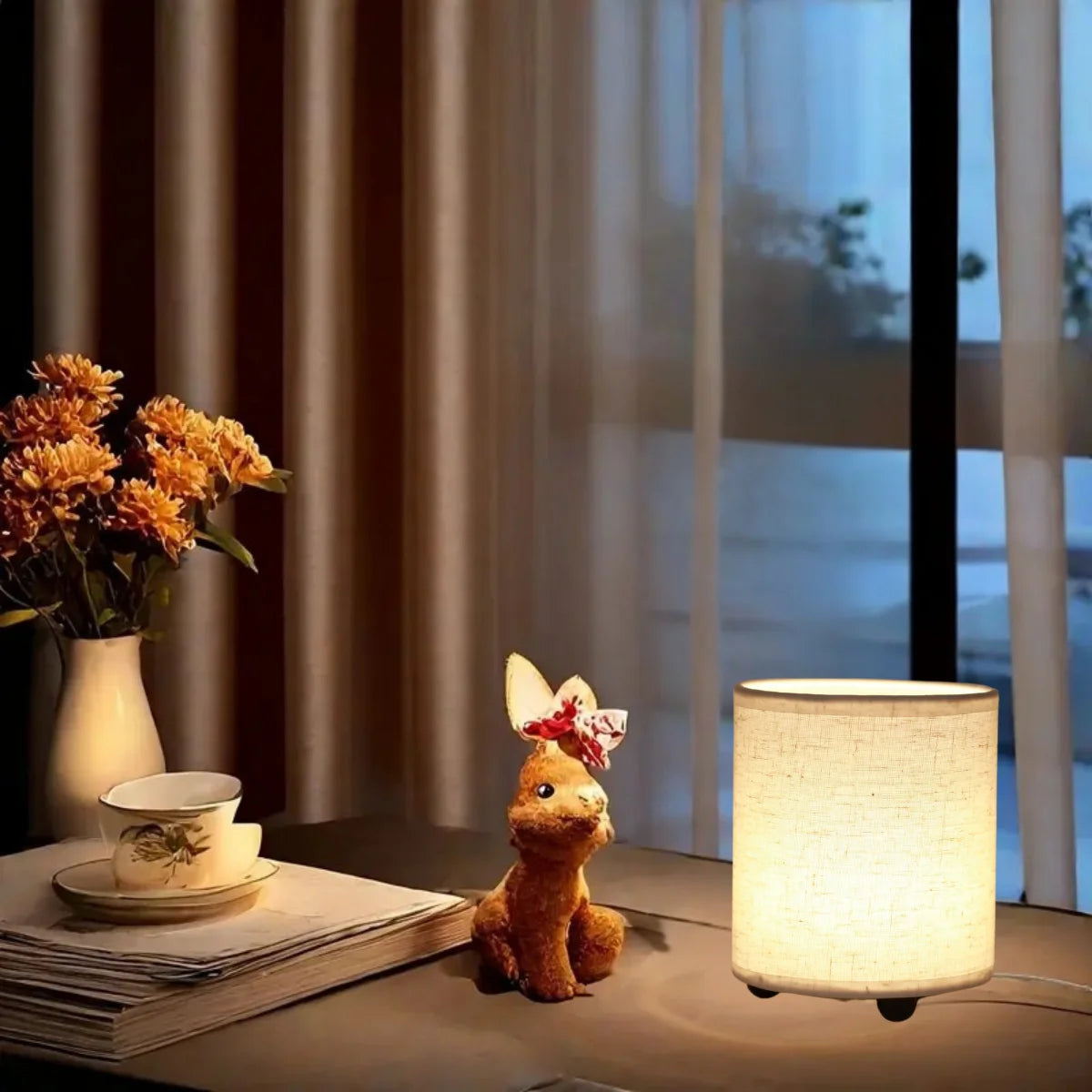A small, golden-brown figurine sits on a wooden surface next to a modern lamp with a warm glow.