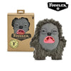 A gray monster plush toy with large eyes and pink funny teeth is shown next to its packaging.