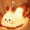 A glowing white silicone rabbit night light is held in a person's hand, illuminating the surrounding area.