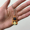 An adorable capybara keychain charm hanging from a silver split ring on a person's hand.