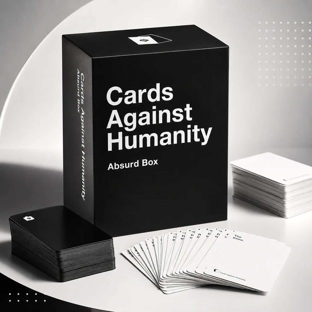A black box of Cards Against Humanity Absurd Box party game with several cards laid out on a white surface.