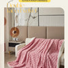A pink velvet blanket draped over a beige sofa in a bright, modern living room setting.