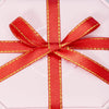 Red satin ribbon tied in a bow with gold edges, displayed on a white gift box.