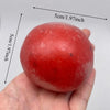 A hand holds a smooth, round, red squishy stress relief fidget ball with measurement lines visible.