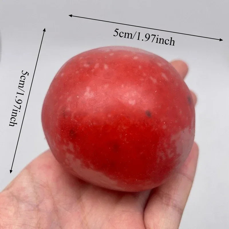 A hand holds a smooth, round, red squishy stress relief fidget ball with measurement lines visible.