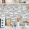 A kitchen backsplash featuring gray and white marble tile stickers above a white countertop.