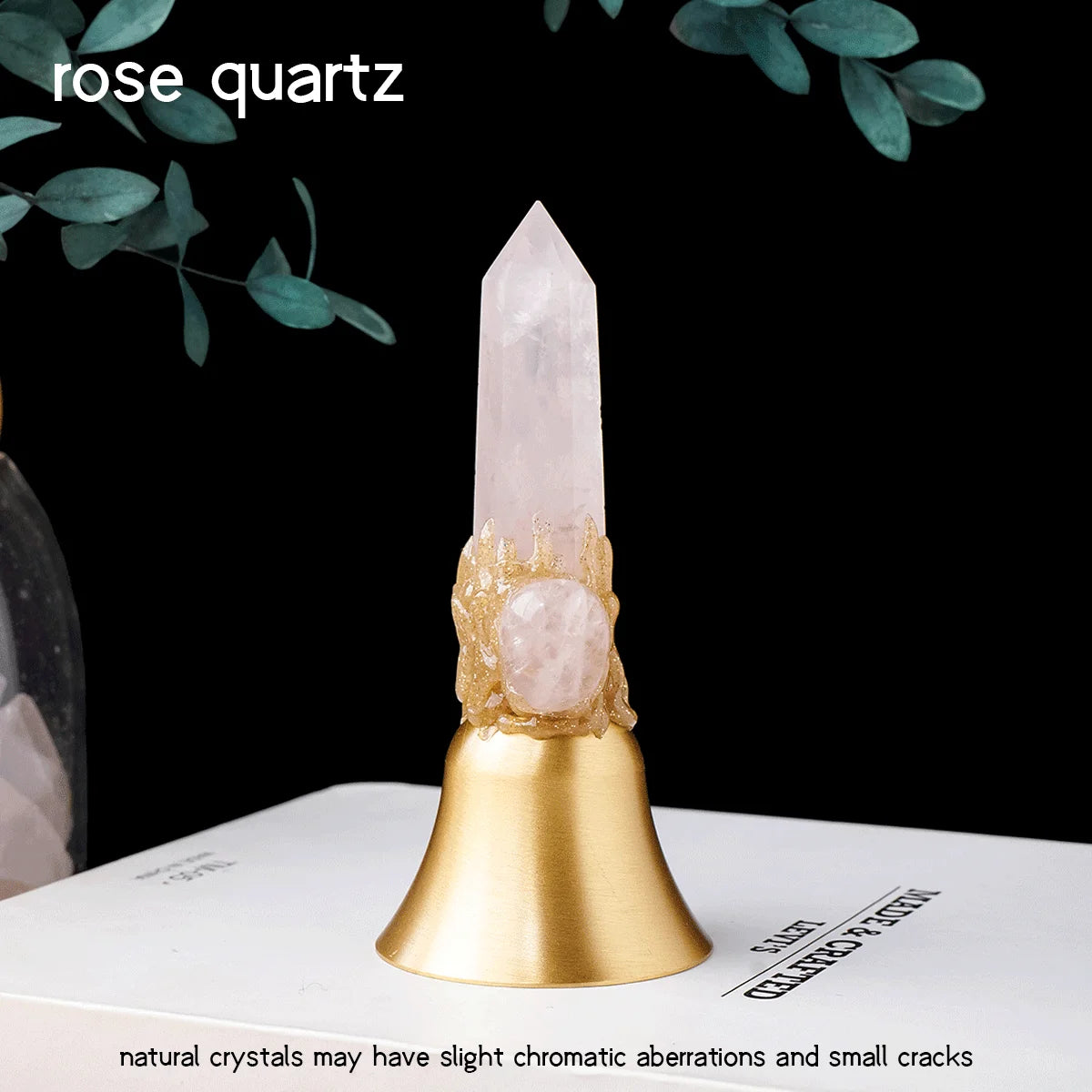 A clear rose quartz crystal point mounted on a brass bell, set against a dark background.