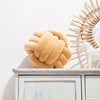 A golden-brown, hand-knotted velvet throw pillow resting on a white wooden cabinet.