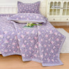 Purple floral quilted bedspread with pink flowers displayed on a bed.