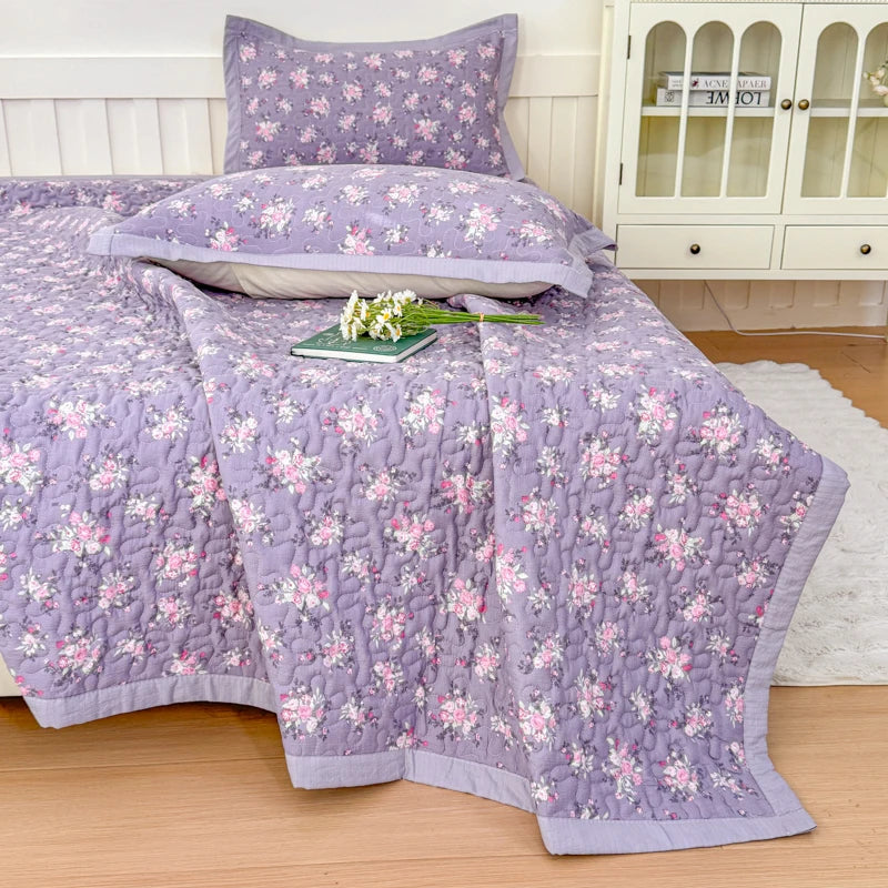 Purple floral quilted bedspread with pink flowers displayed on a bed.