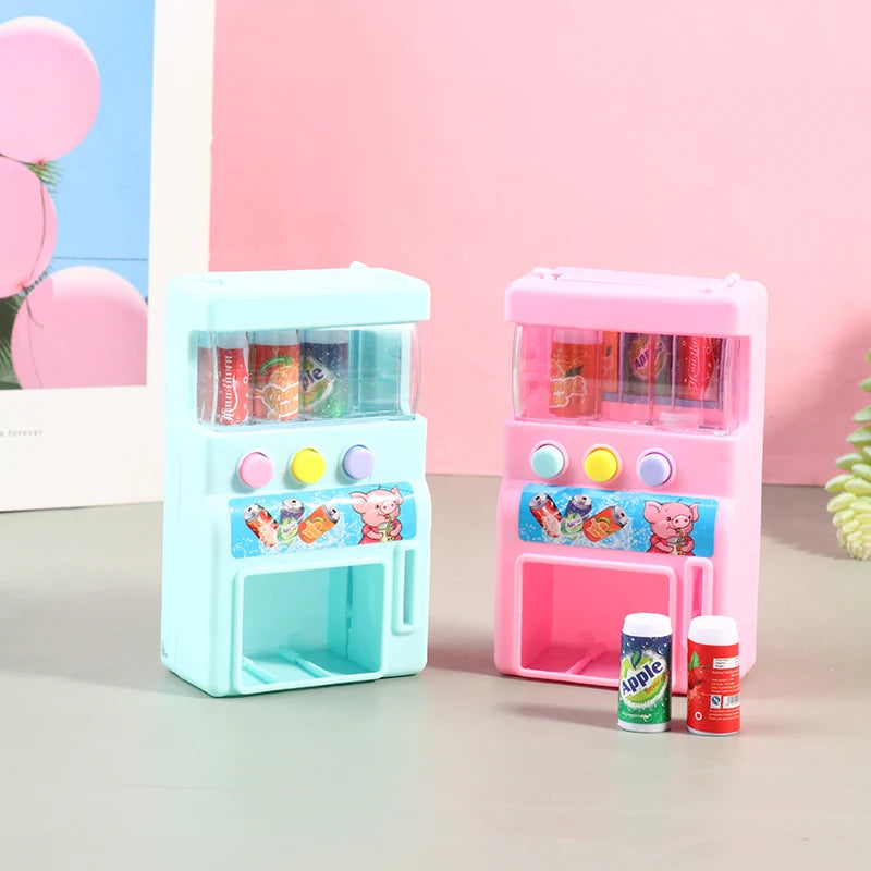 A pink interactive vending machine toy with clear compartments for play coins and drinks sits on a gray surface.
