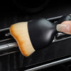 A close-up of a black and natural fiber detailing brush being held over a car vent or gap.
