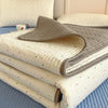 A stack of floral quilted bedspreads in light cream and gray tones resting on a blue surface.