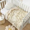 A cream-colored baby swaddle blanket with a bear print, draped over a white wooden crib.