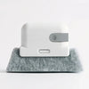 A white groove cleaning brush with a gray replaceable scouring head resting on a gray felt surface.
