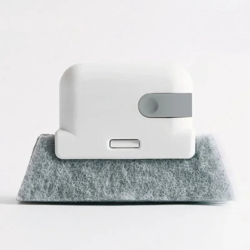 A white groove cleaning brush with a gray replaceable scouring head resting on a gray felt surface.