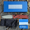 A blue box, a folding knife, and a black sheath with an Axis brand logo are displayed on wood.