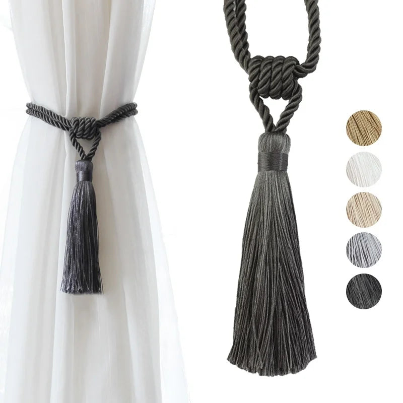 A set of two dark gray tassel curtain tiebacks with braided cord for holding fabric.