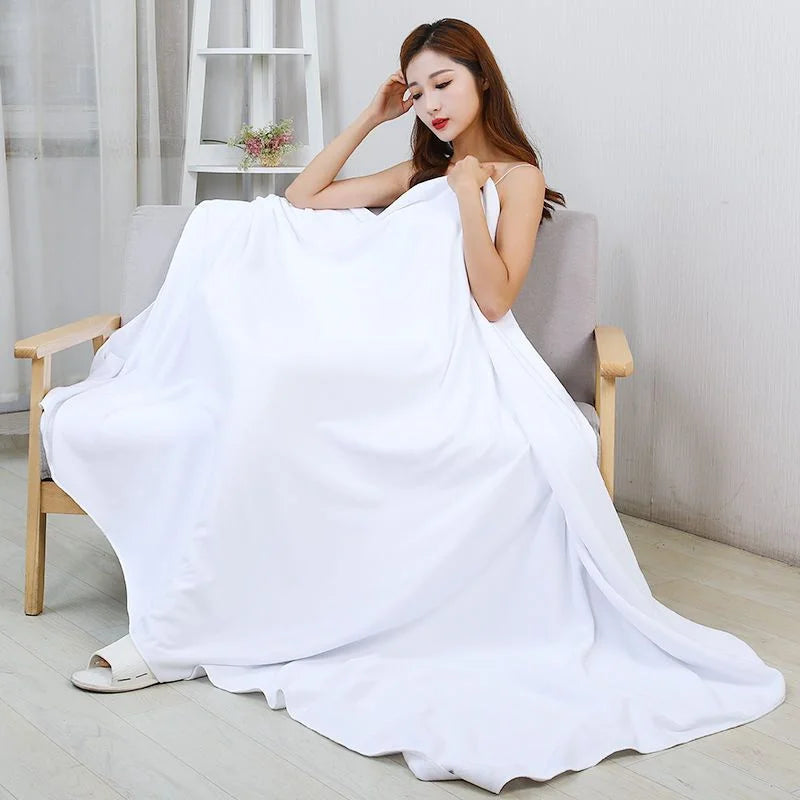 A woman is draped in a large white microfiber bath towel, showcasing its soft texture and absorbency.