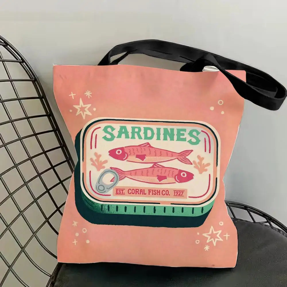 A pink canvas tote bag featuring a graphic print of sardines and text indicating the establishment date.