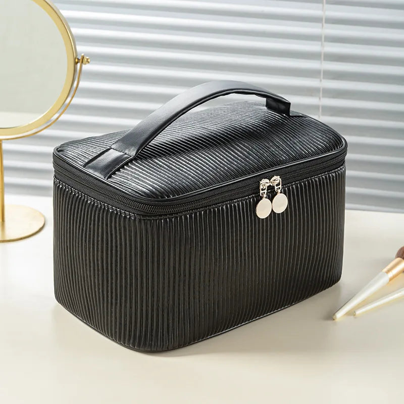 A black PU leather makeup bag set with a handle and silver earrings is displayed on a light surface.