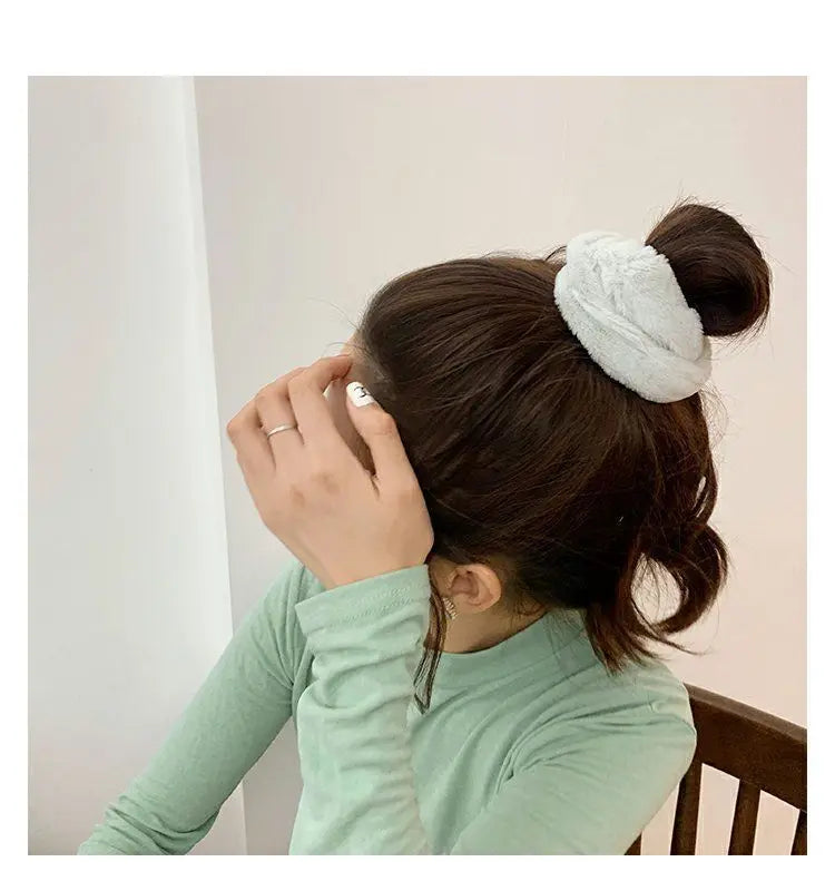 A woman ties her dark hair with a white plush coil hair tie.
