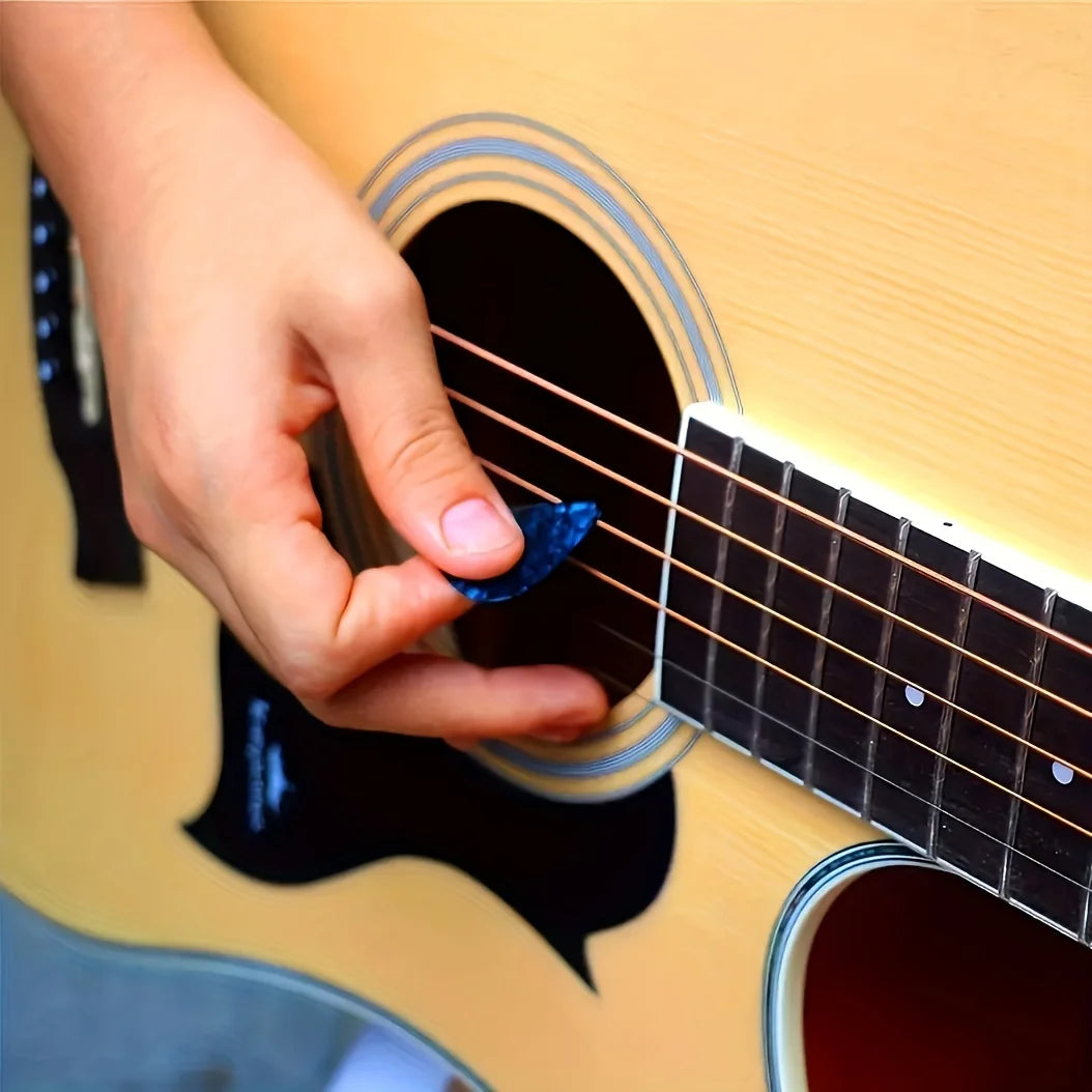 A hand is playing a guitar with assorted picks on a yellow wooden surface.