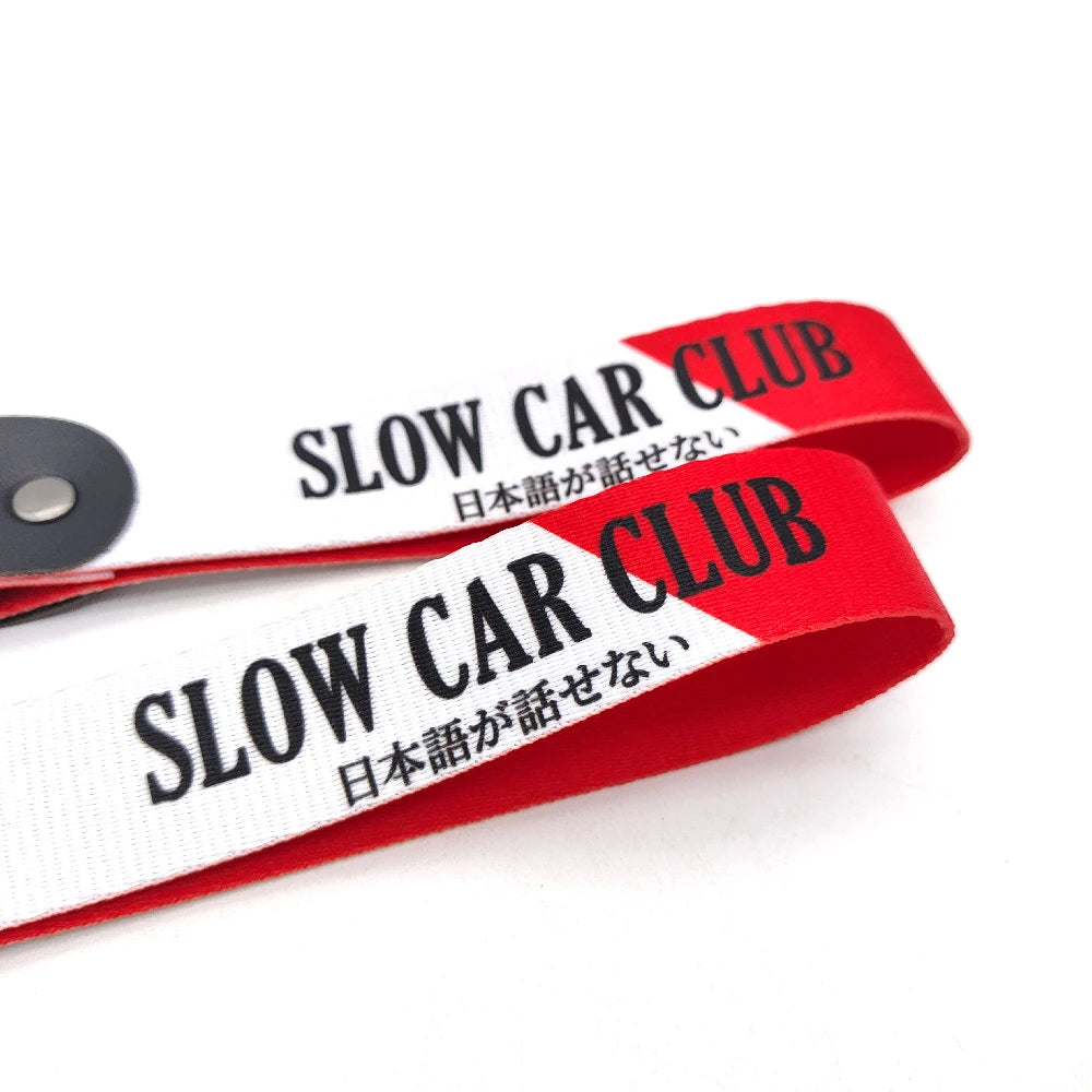 Red and white striped fabric ribbon with black text reading SLOW CAR CLUB and Japanese characters on a nylon keychain.