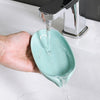A hand is pouring water into a leaf-shaped suction cup soap dish, which is draining into a sink.