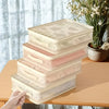 A stack of foldable bedding storage bags in light beige and pink tones resting on a wooden table.