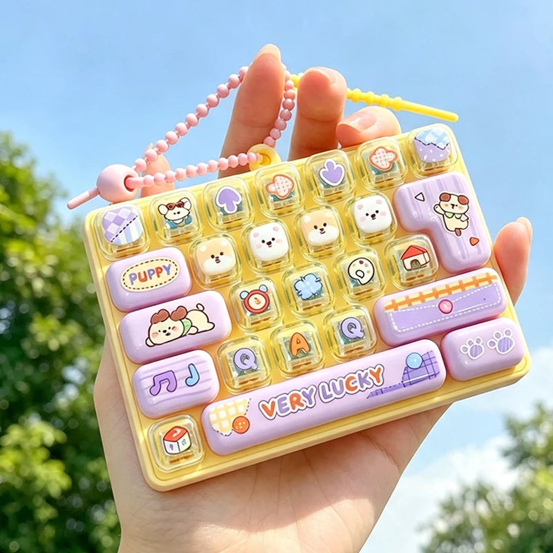 A hand holds a yellow fidget keychain featuring purple and white cartoon keycaps and pink beaded chains.