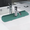 A chrome silicone faucet drain mat is placed on a white countertop next to a modern kitchen or bathroom sink.